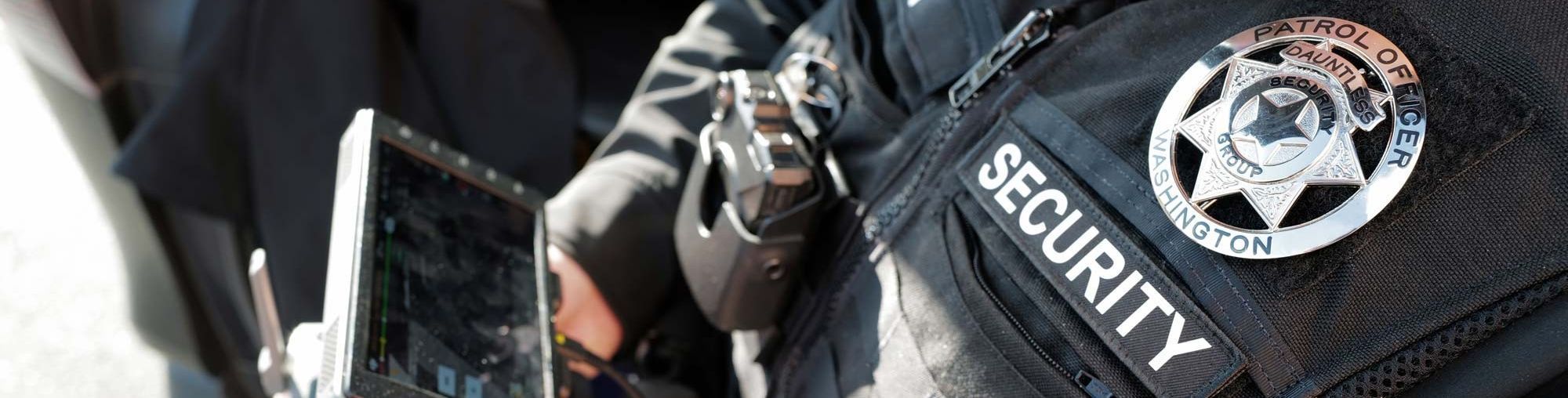 Close up of a security guard in uniform displaying their badge, title and vest camera prominently.