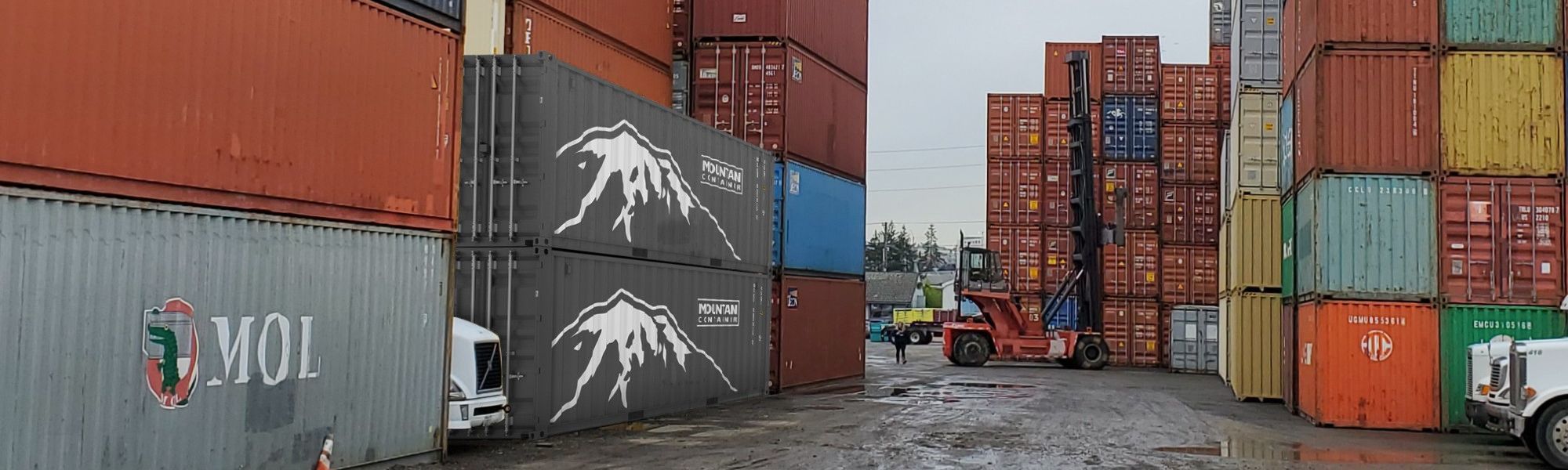 Multiple brands of shipping containers stacked on top of one another in a shipping container yard with a forklift driving by.