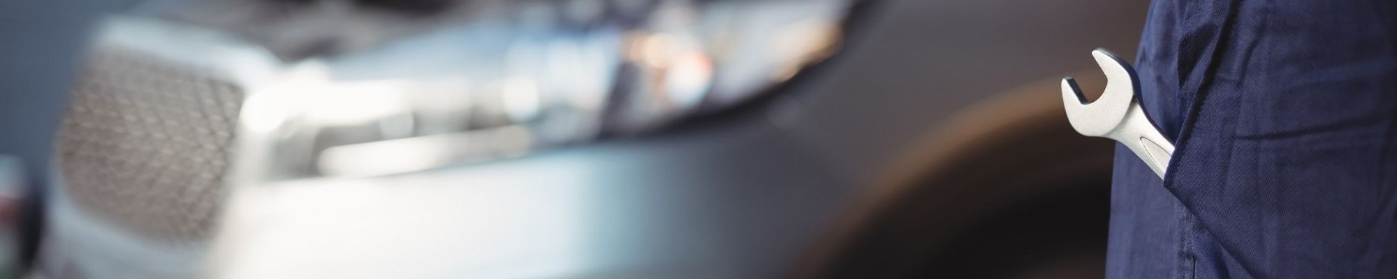 Man in work overalls with a close up of his pocket that has a wrench in it with a sliver SUV blurred in the background.