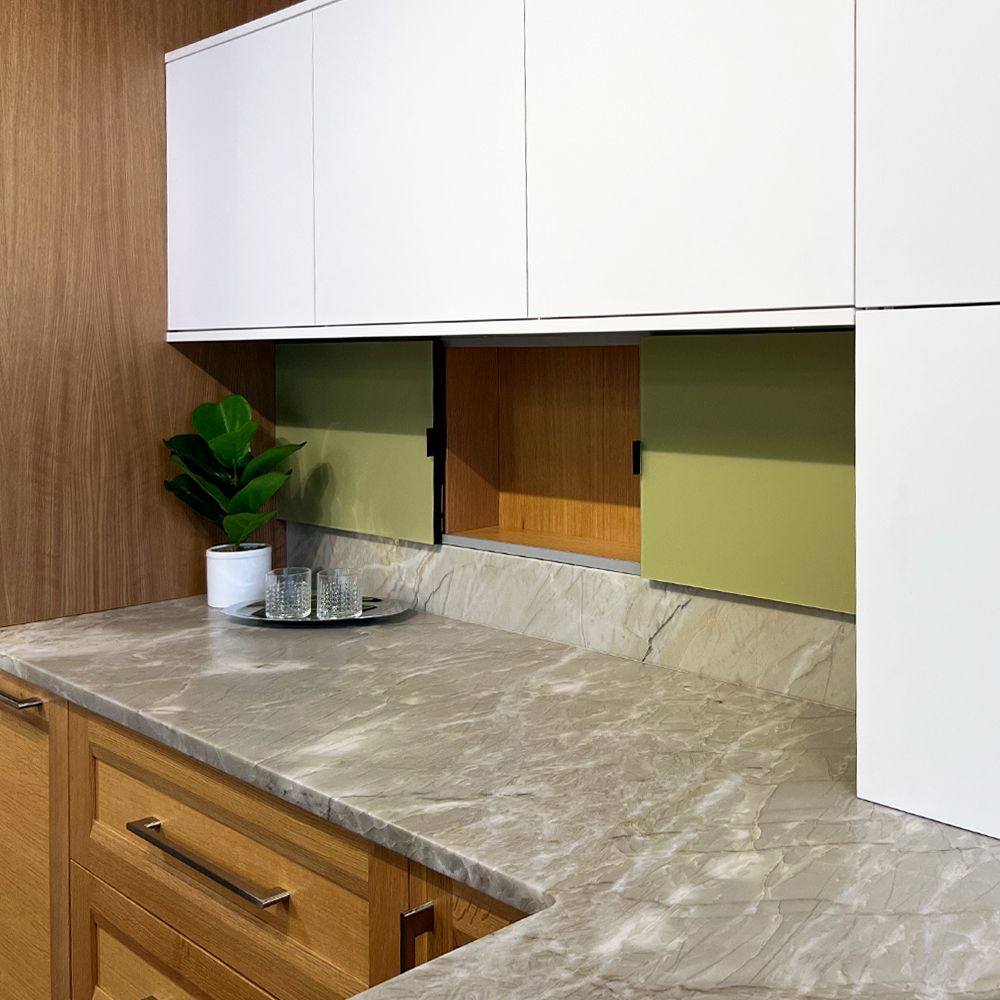 Close up of kitchen cabinets and countertop. Lower cabinets are wood, upper cabinets are white and the countertop is a grey silver stone. There are small middle cabinets with light green doors. 