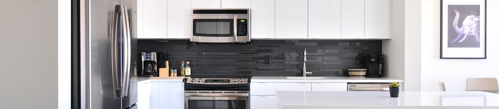 Closeup image of a renovated kitchen with white cabinets and countertops, grey backsplash and gleaming silver appliances. 