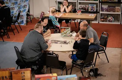 Group of men and one boy playing a table top game in the game room at Kingcon