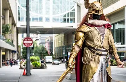 Cosplayer in Full gold armor posing standing up with a sword in front of a building