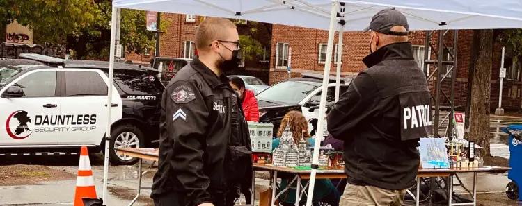 Two Dauntless security officers standing guard at an event with a Dauntless patrol vehicle visible in the background.