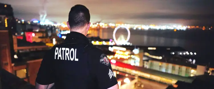 Patrol officer overlooking downtown Seattle from a rooftop at night with city lights in the background.