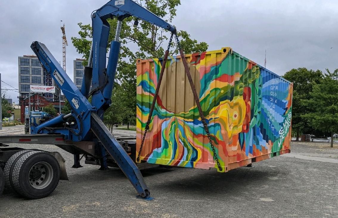 Colorful seahawks shipping container being offloaded from a semi-truck using a side lifter.