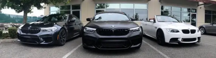 Three sport BMW cars in a parking lot. The left is jet black, the middle is matte black and the right is a convertible in white.