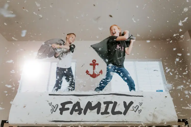 2 kids jumping on a bed having a pillow fight