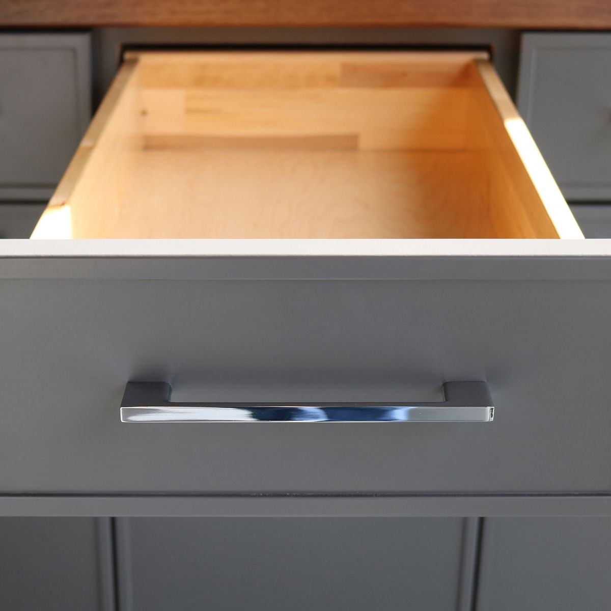 Close up of open grey cabinet drawer with silver handle, inside of the drawer is a light-colored wood