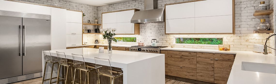 Kitchen with white brick backsplash, smooth white cabinet faces and counter tops with wood accents.  Silver appliance 