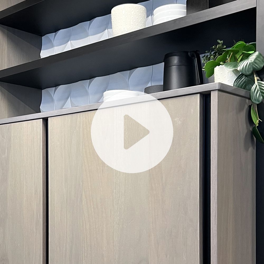 Close up of cabinets. Grey wood cabinet faces with no handles with black open face shelved above with white dishes. 