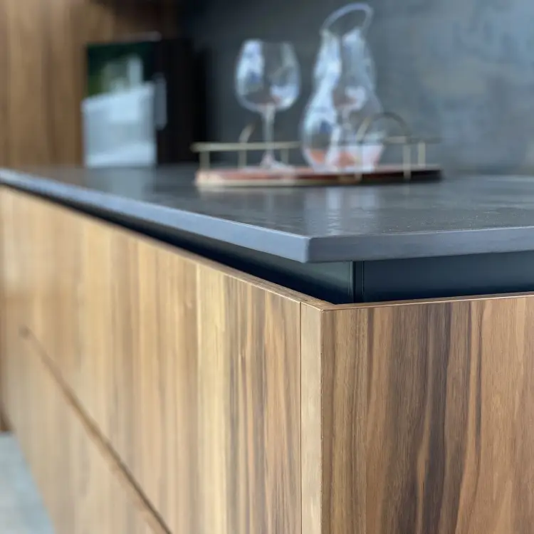 Close up of the corner of a kitchen counter, wood drawers, stone countertop with a glass pitcher and wine glass on a tray.