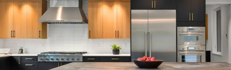 Modern kitchen with white tile backsplash, half wood half black cabinets with gold and black handles and silver appliances 