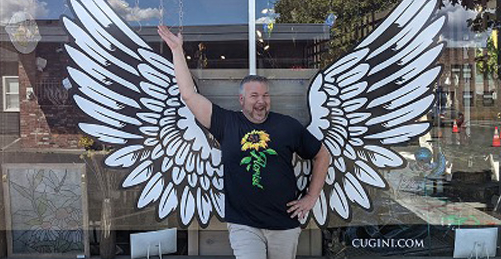 owner of Cugini Florist stnading in front of store by angel mural on window