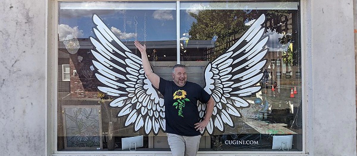 Owner of Cugini Florists standing in front of window painted with angel wings 