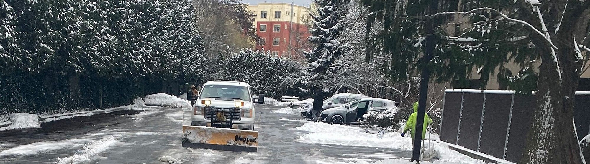 Downtown Kent Washington in winter where an Alamo snow plow pickup truck clears the street of piled up snow. 