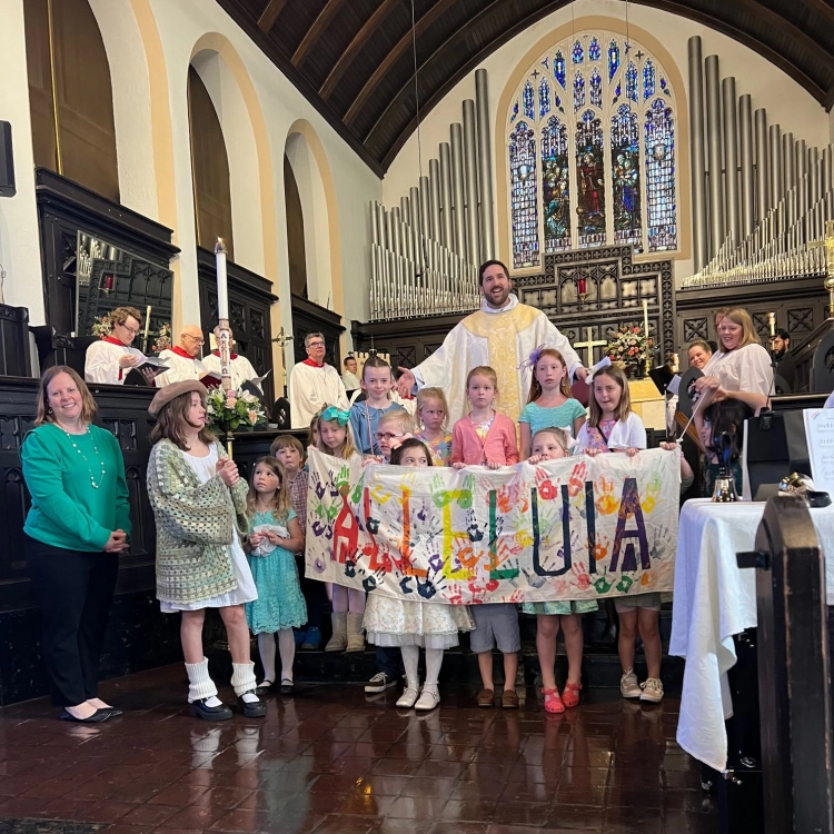 Rev. Charles Cowen and the children of St. Andrew's hold a banner across the steps in the church. The choir is in the background.